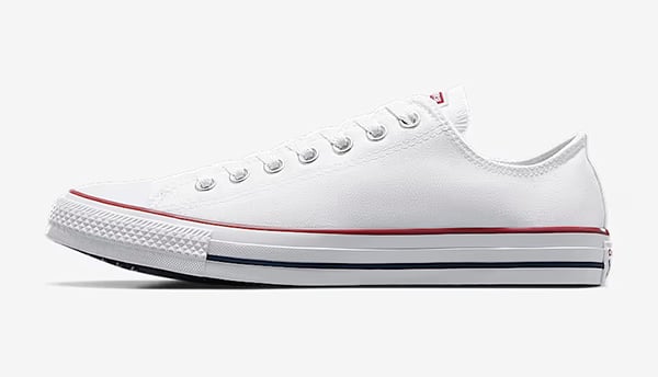 A white low-top canvas sneaker with a rubber sole, metal eyelets, and red and blue stripes along the midsole—perfect men's summer footwear—shown in side profile on a plain background.