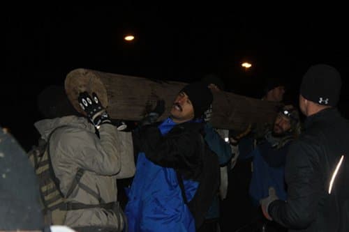 brettlog Man helping the people to carry a log.