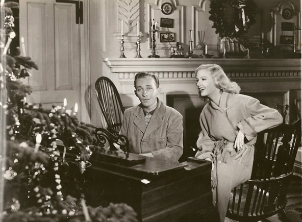 Two people in vintage attire from the 1940s sitting by a piano near a Christmas tree, enjoying classic Christmas songs in a classic black-and-white film scene.