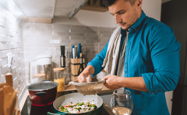 A man in a blue shirt is cooking in the kitchen.
