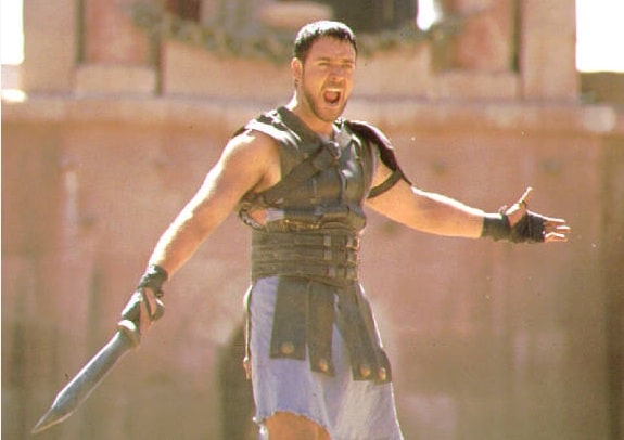 A man in a Roman costume embodying lessons in manliness as a gladiator, solemnly gripping a sword.