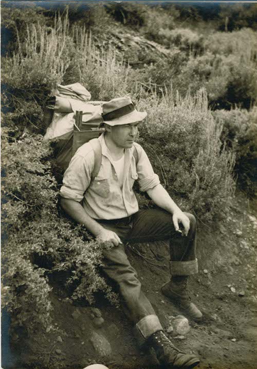 A man engaged in international backpacking, sitting on a hillside with his backpack.