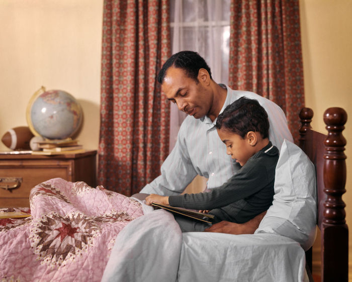 A father and son reading a book together in bed.