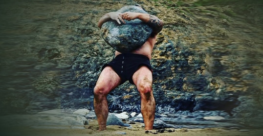 Man lifting an ancient stone outdoors.