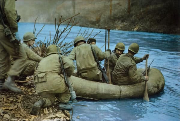 Soldiers in military uniforms using an inflatable raft to cross a river in one of the amazing WWII photos.