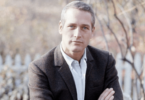 A casual man sits on a bench with his arms crossed.